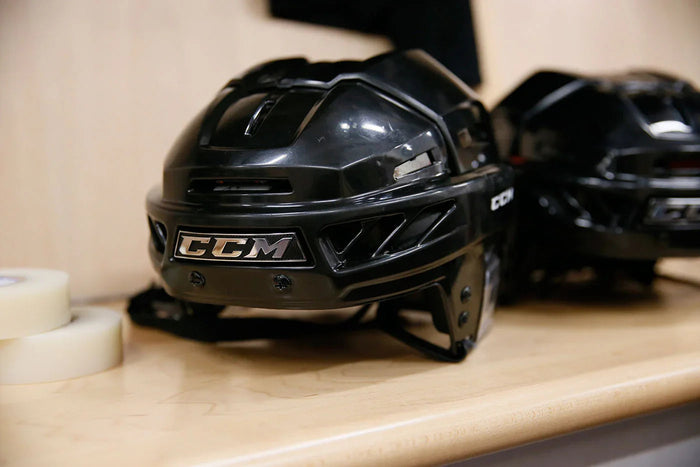 Black CCM hockey helmet on locker room bench, hockey equipment at TheHockeyShop.com