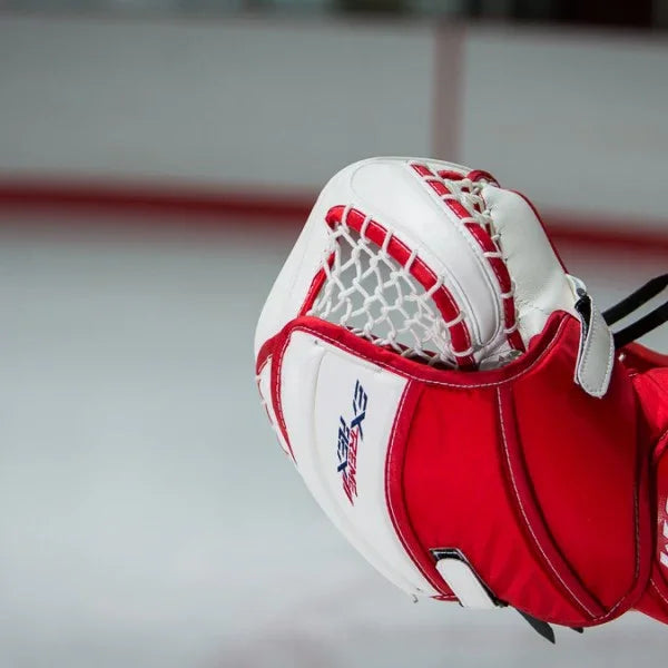 Red and white CCM hockey goalie glove on ice rink, available at TheHockeyShop.com