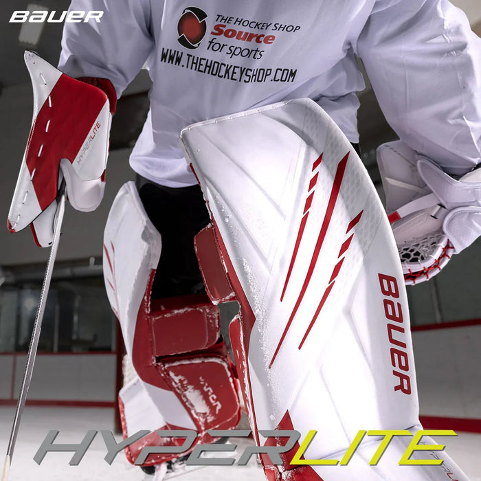 Bauer Hyperlite goalie leg pads in red and white on ice, The Hockey Shop branding visible.