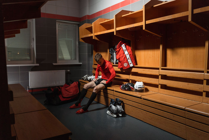 Young hockey player sitting alone on the locker room bench with his gear after a game