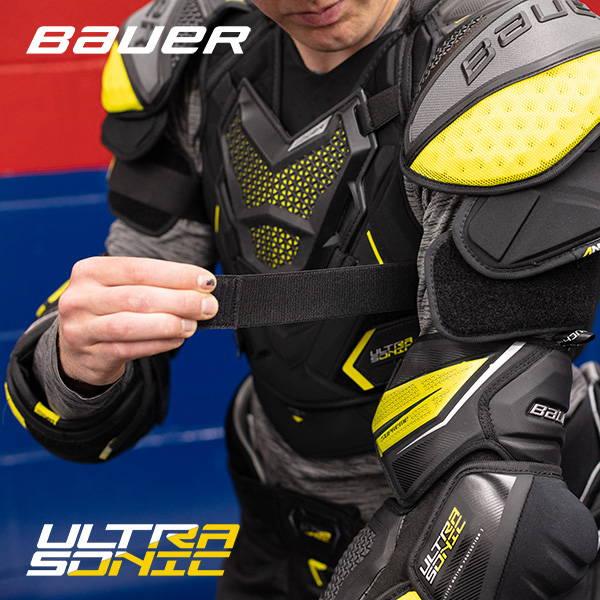Hockey player adjusting Bauer Ultrasonic hockey shoulder and elbow pads in locker room