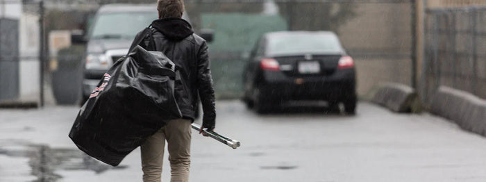 Hockey player carrying large hockey equipment bag and sticks in rainy parking lot