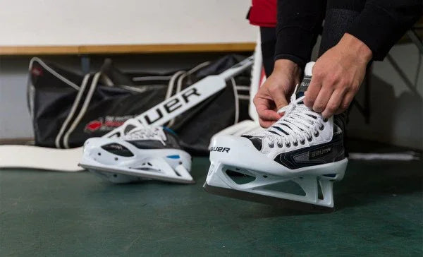 Person lacing up Bauer Reactor 9000 hockey skates beside Bauer hockey bag at TheHockeyShop.com