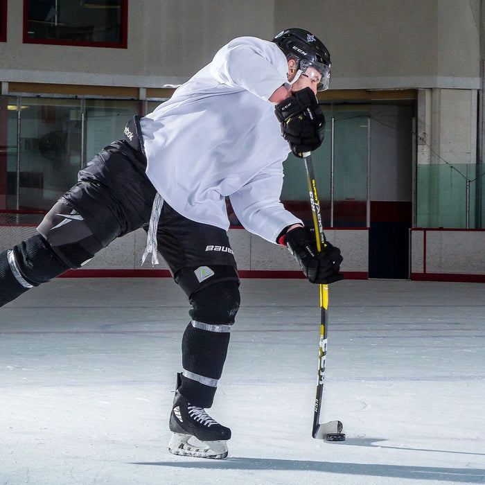Hockey player in CCM gear shooting puck on ice rink, showcasing TheHockeyShop equipment.