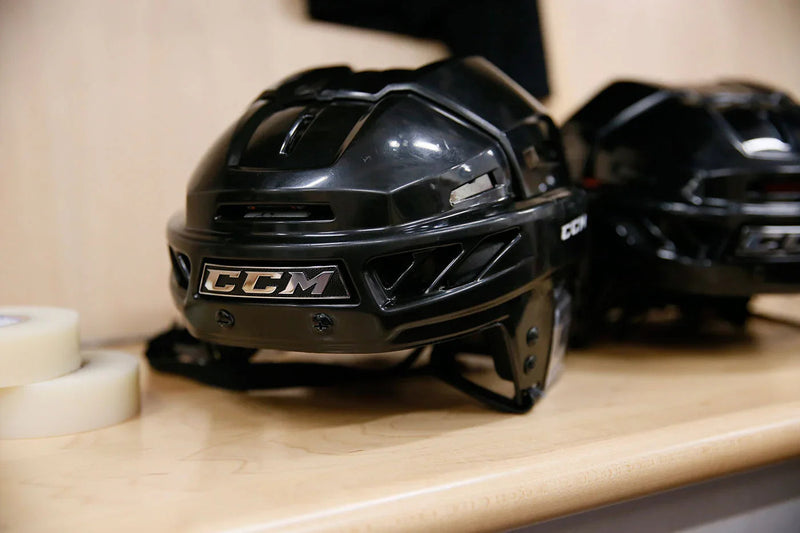 Black CCM hockey helmet on locker room bench, hockey equipment at TheHockeyShop.com