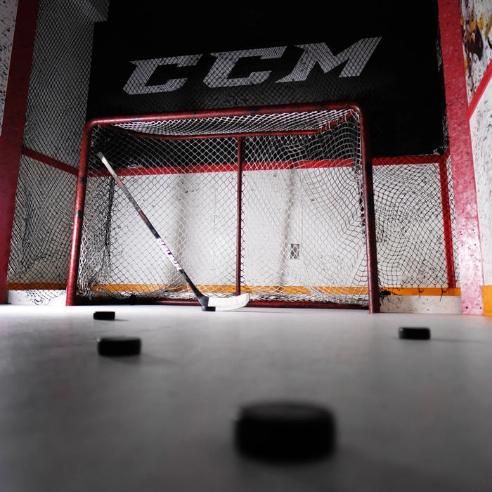 Hockey net with CCM branding, stick, and pucks on ice at The Hockey Shop