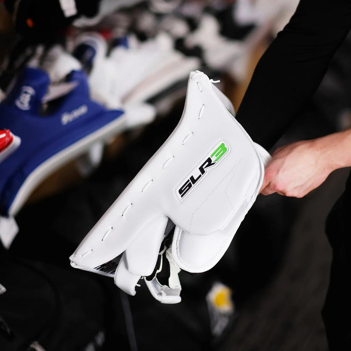 Person holding white SLR3 hockey goalie blocker at The Hockey Shop equipment display