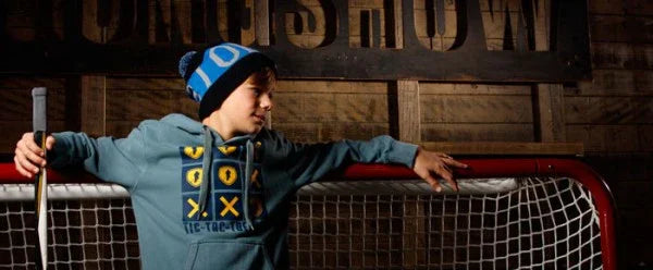 Youth in blue hockey hoodie and beanie leaning on hockey net at The Hockey Shop rink