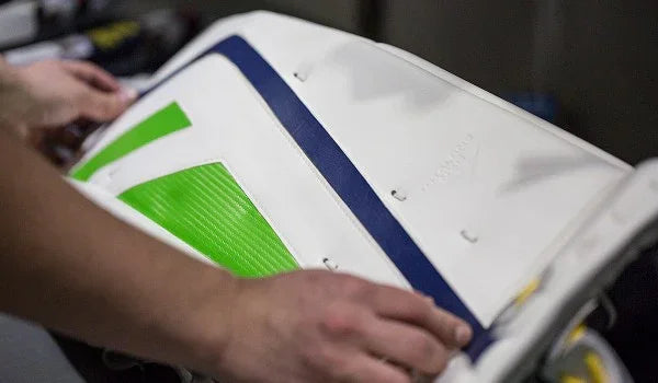 Applying green and blue PadSkinz to white hockey goalie leg pad at The Hockey Shop