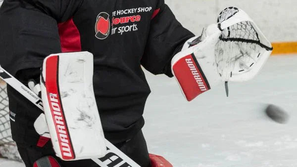 Hockey goalie wearing Warrior blocker and catcher on ice, The Hockey Shop gear visible