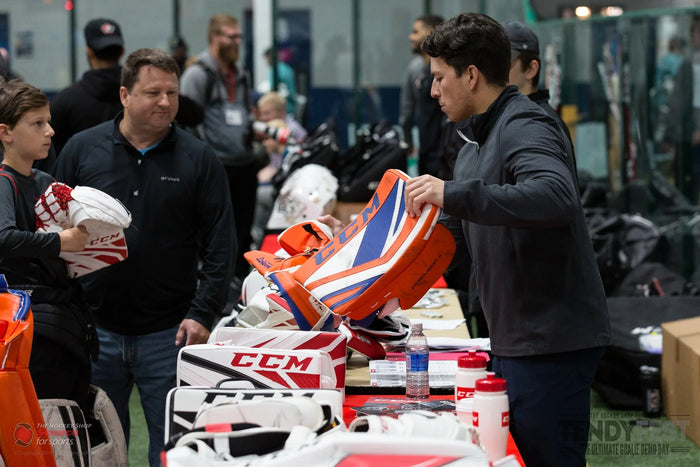 Shoppers examining CCM goalie pads at The Hockey Shop event, with hockey equipment on display.