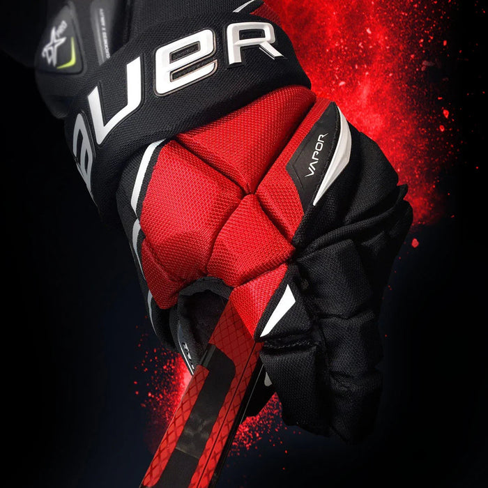 Bauer Vapor hockey glove gripping a red and black stick with red splash background