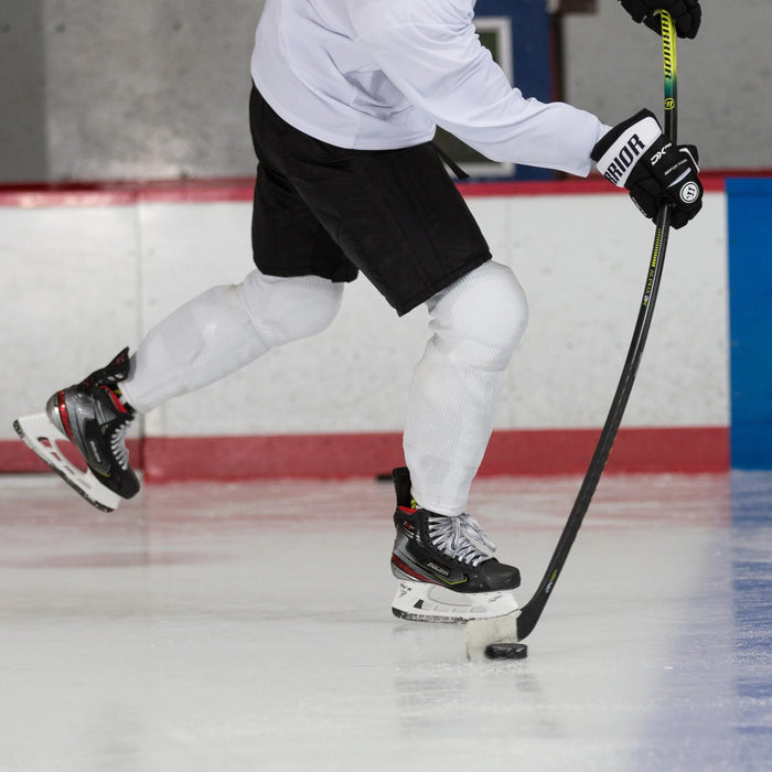 Hockey player using Warrior Alpha DX stick on ice rink, wearing Bauer skates and gear