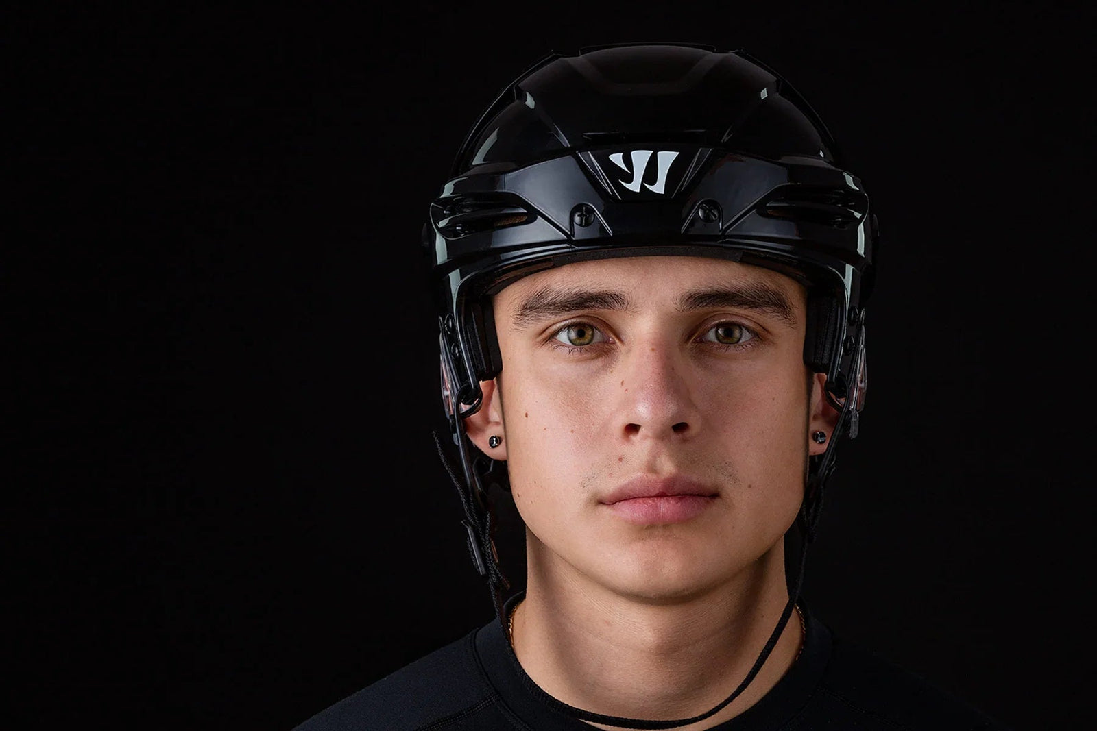 Male hockey player wearing black Warrior Krown hockey helmet, close-up on black background