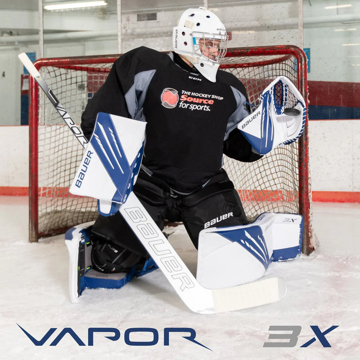 Bauer Vapor 3X goalie in blue and white gear blocking net on ice at The Hockey Shop rink.