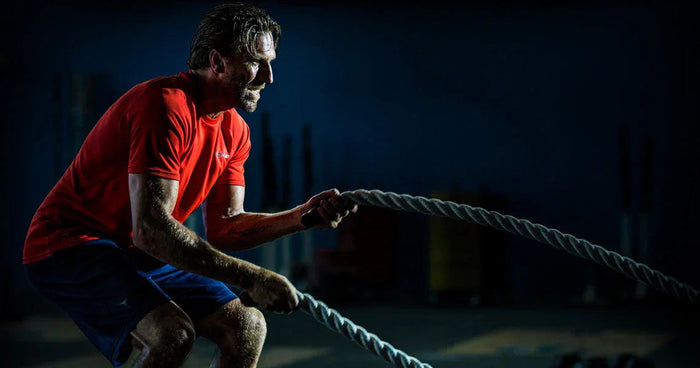 Man training with battle ropes in gym, wearing Bauer shirt, hockey equipment fitness