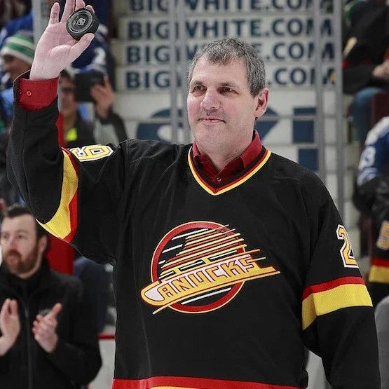 Man in vintage Vancouver Canucks jersey holding hockey puck at arena event, TheHockeyShop.com