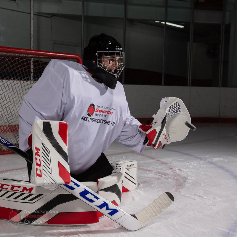 Hockey goalie in CCM Axis gear making a save on ice, TheHockeyShop.com branding visible.