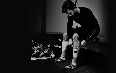 Hockey player in locker room putting on socks with skates and gear beside bench at The Hockey Shop