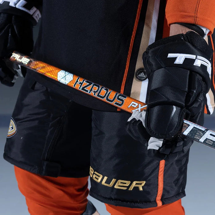 Close-up of a hockey player in Bauer shorts, orange pants, True gloves, holding HZRDUS PX stick