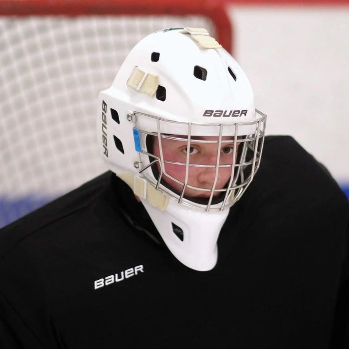 Hockey goalie wearing Bauer mask and gear on ice rink in front of goal net