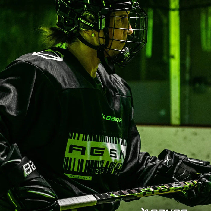 Hockey player in black Bauer gear holding a stick on an indoor ice rink, TheHockeyShop.com