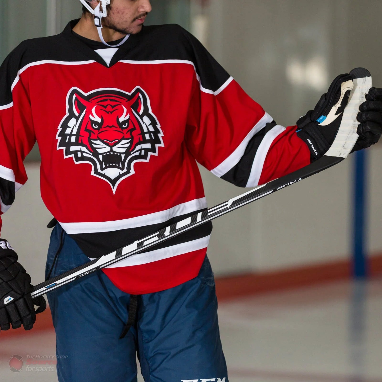 Hockey player in red jersey with tiger logo holding True XC9 stick on ice, TheHockeyShop.com